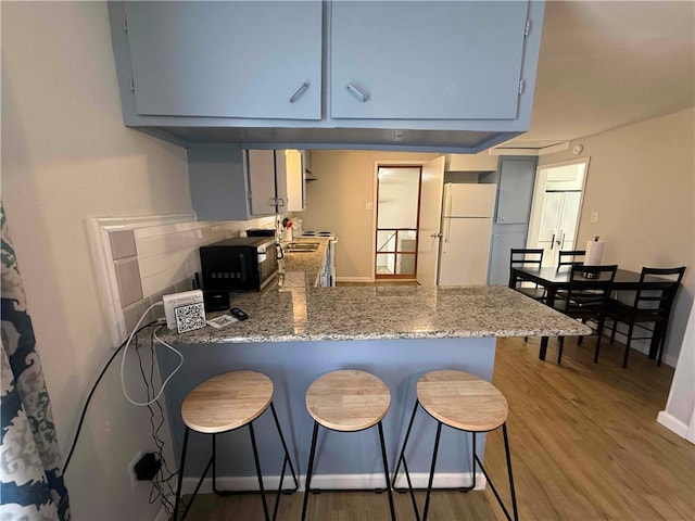 kitchen with kitchen peninsula, white fridge, stone countertops, gray cabinets, and hardwood / wood-style flooring