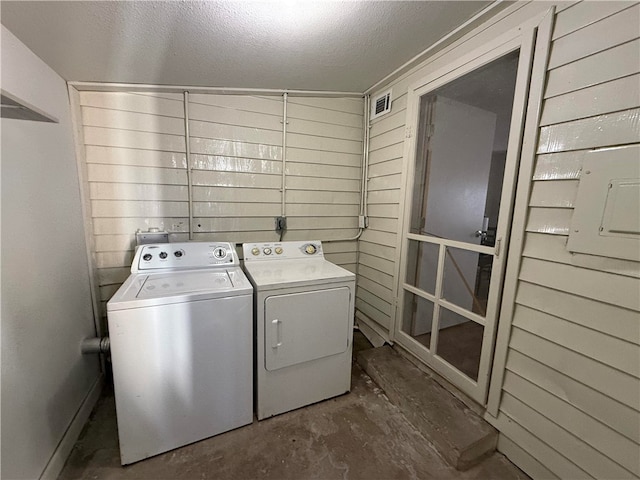 laundry area featuring a textured ceiling, washer and clothes dryer, and wood walls