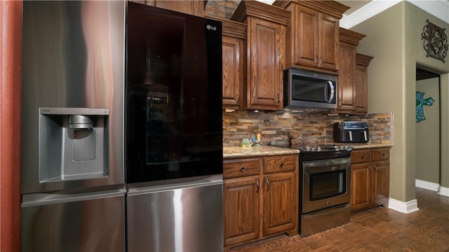 kitchen with stainless steel appliances, ornamental molding, tasteful backsplash, light stone countertops, and dark hardwood / wood-style flooring