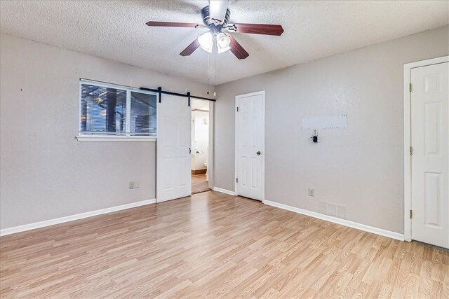 10502 Hemlock Rd, Corpus Christi, TX 78410 - unfurnished bedroom with light wood-type flooring, a barn door, a textured ceiling, and ceiling fan
