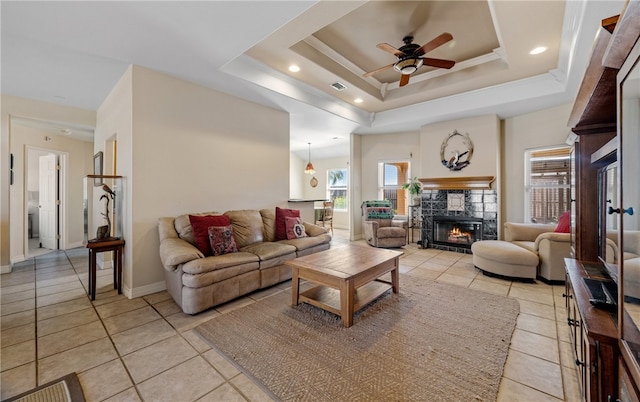 living area featuring light tile patterned floors, a glass covered fireplace, a raised ceiling, and a ceiling fan