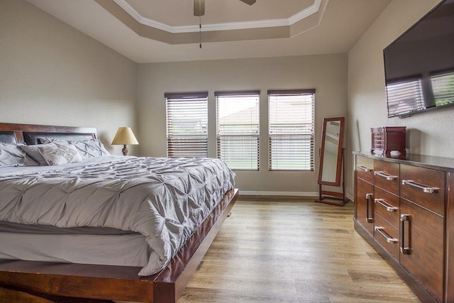 bedroom with baseboards, light wood-style flooring, ceiling fan, a tray ceiling, and crown molding