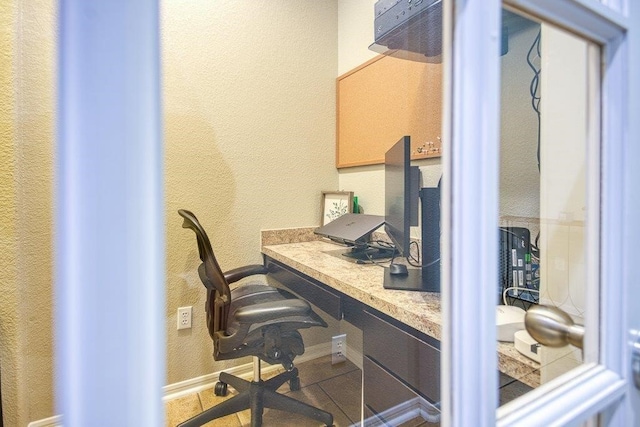 office featuring baseboards, built in desk, and a textured wall