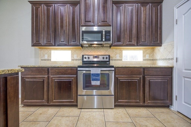 kitchen with light tile patterned floors, dark brown cabinets, appliances with stainless steel finishes, backsplash, and light stone countertops