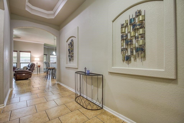 corridor with baseboards, arched walkways, stone tile floors, and crown molding