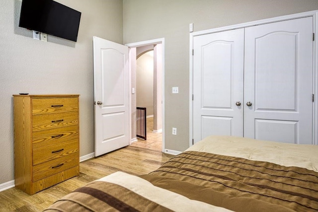 unfurnished bedroom featuring arched walkways, a closet, baseboards, and light wood finished floors