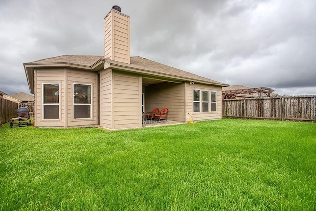 back of house with a fenced backyard, a chimney, and a yard