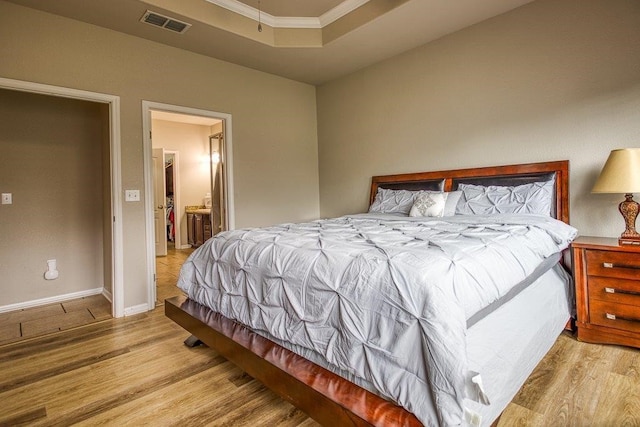 bedroom featuring light wood-style floors, a tray ceiling, visible vents, and baseboards