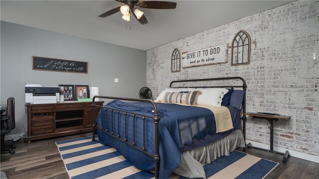 bedroom with dark wood-type flooring, ceiling fan, and brick wall