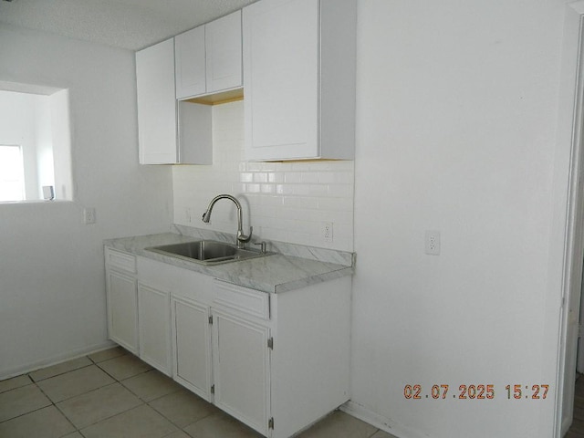 kitchen featuring backsplash, light tile patterned floors, sink, and white cabinets