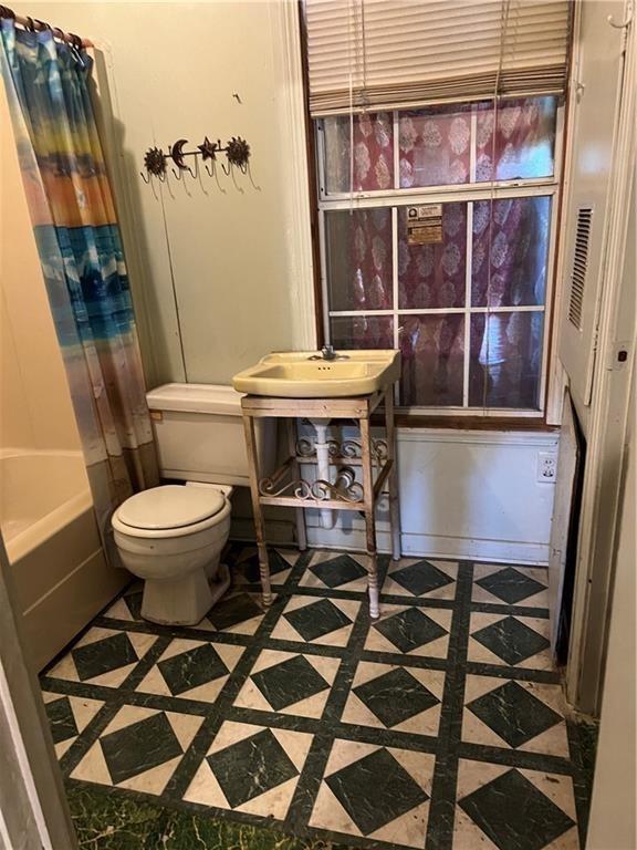 bathroom featuring toilet and shower / bathtub combination with curtain