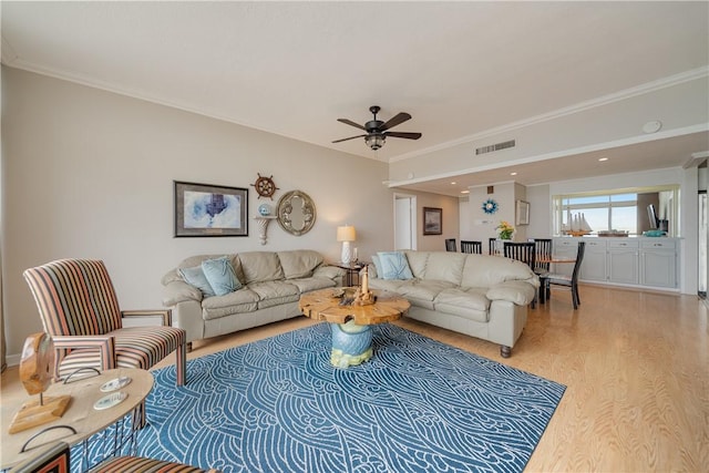 living area with light wood-style flooring, crown molding, and a ceiling fan