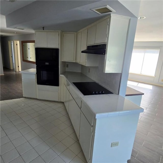 kitchen featuring light tile patterned floors, under cabinet range hood, light countertops, black appliances, and tasteful backsplash