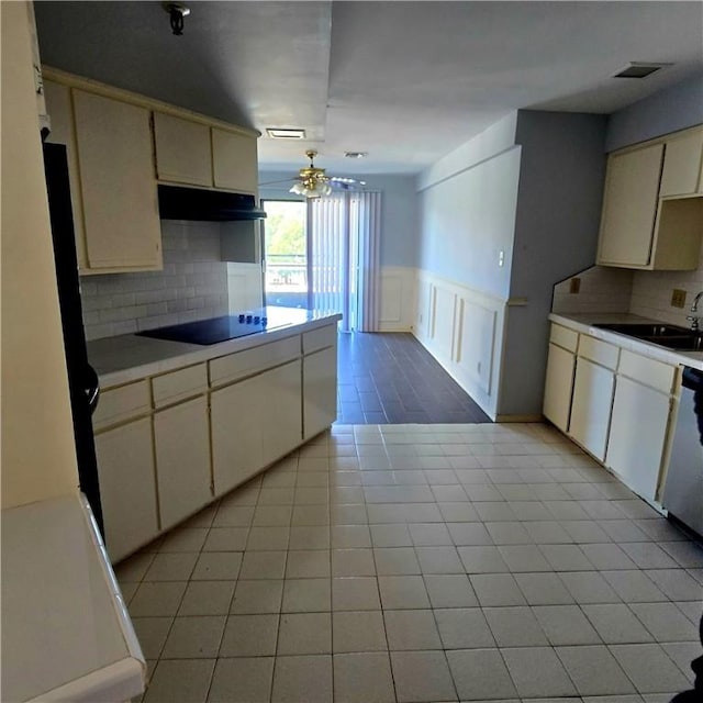 kitchen featuring a wainscoted wall, light countertops, black electric cooktop, under cabinet range hood, and a sink