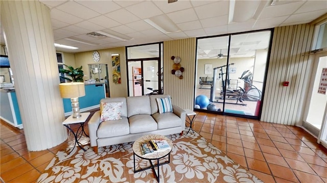 living room with wooden walls, light tile patterned floors, and a drop ceiling