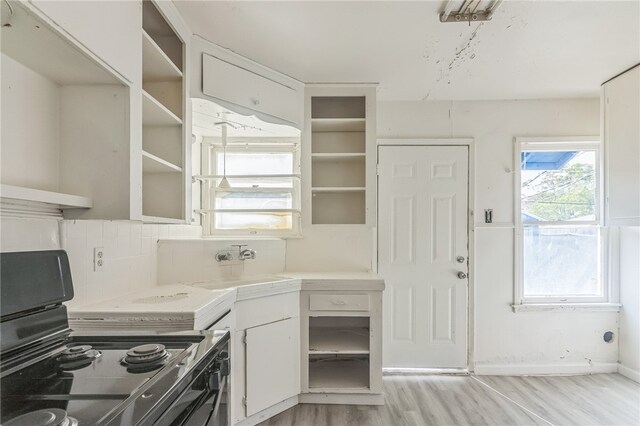 kitchen with white cabinets, light hardwood / wood-style floors, black electric range oven, and decorative backsplash