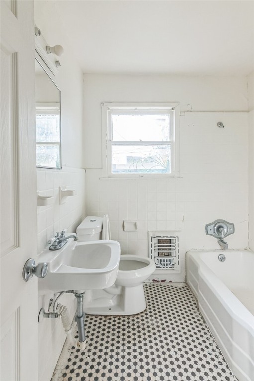 bathroom with tile patterned flooring, heating unit, toilet, and tile walls