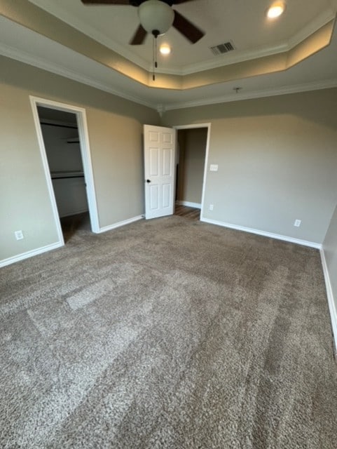 unfurnished bedroom with ornamental molding, carpet, ceiling fan, and a tray ceiling