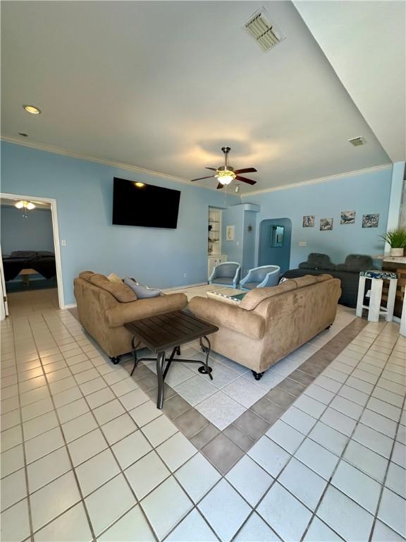 living room with ceiling fan, light tile patterned floors, visible vents, and ornamental molding