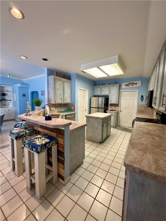 kitchen featuring light tile patterned floors, a kitchen island, a peninsula, a sink, and appliances with stainless steel finishes