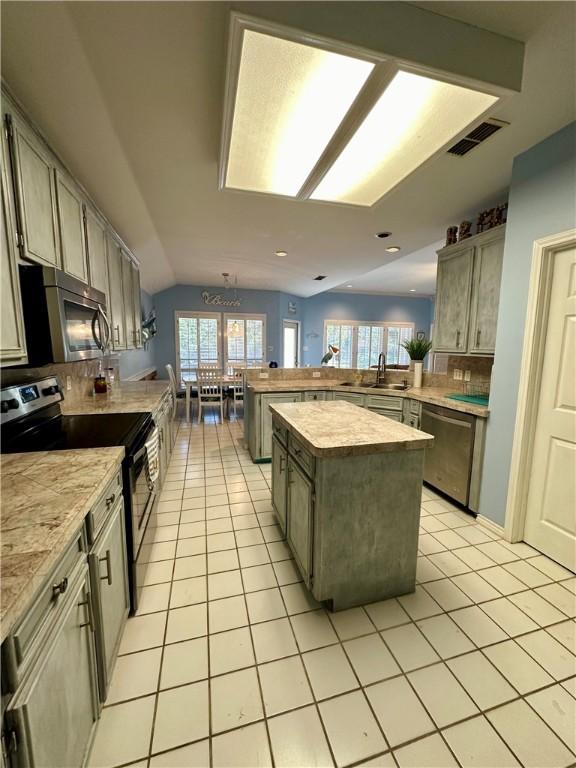 kitchen featuring visible vents, lofted ceiling, a peninsula, light tile patterned flooring, and appliances with stainless steel finishes