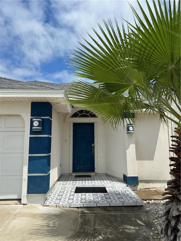 view of exterior entry featuring stucco siding, an attached garage, and roof with shingles