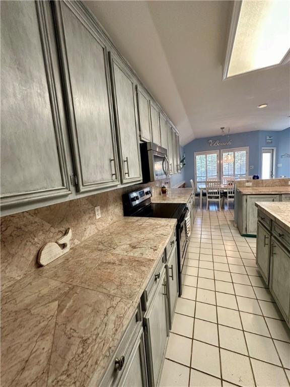 kitchen with stainless steel appliances, a peninsula, light tile patterned floors, decorative backsplash, and vaulted ceiling