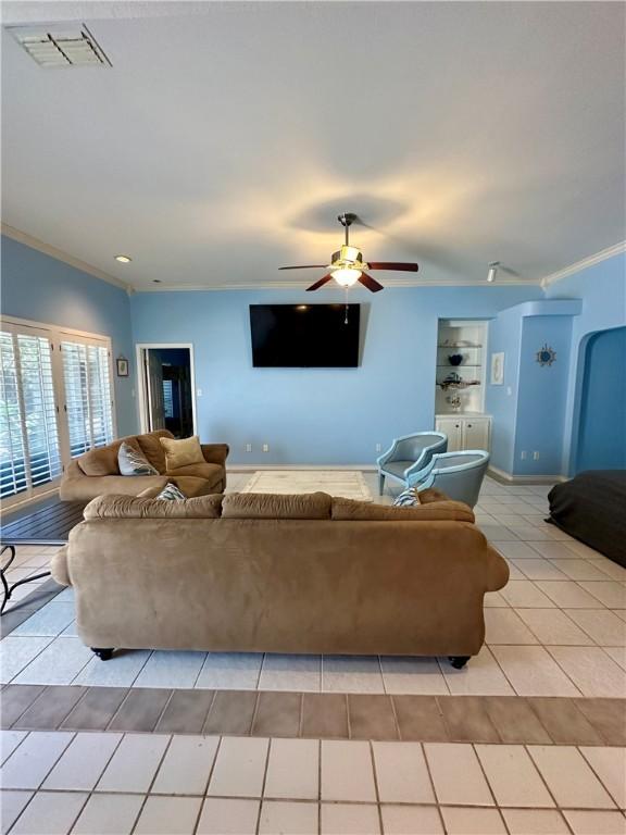 living room featuring light tile patterned floors, a ceiling fan, visible vents, baseboards, and crown molding