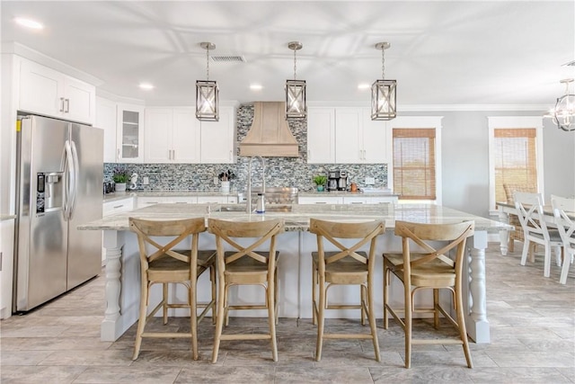 356 E Sagebrush St, Rockport, TX 78382 - kitchen with stainless steel fridge with ice dispenser, custom range hood, crown molding, backsplash, and a kitchen island with sink