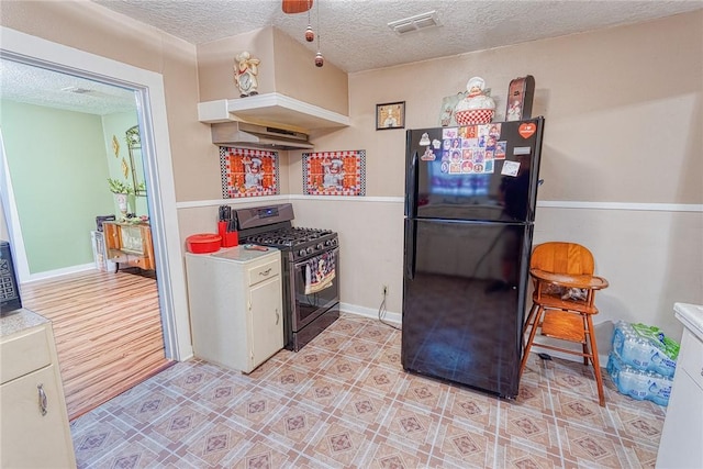 kitchen with black refrigerator, white cabinetry, gas range, and a textured ceiling