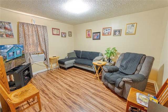 living room featuring a wall mounted air conditioner, a textured ceiling, and light wood-type flooring