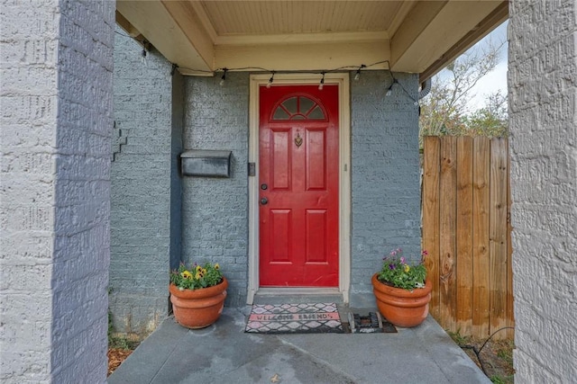 view of exterior entry featuring fence and brick siding