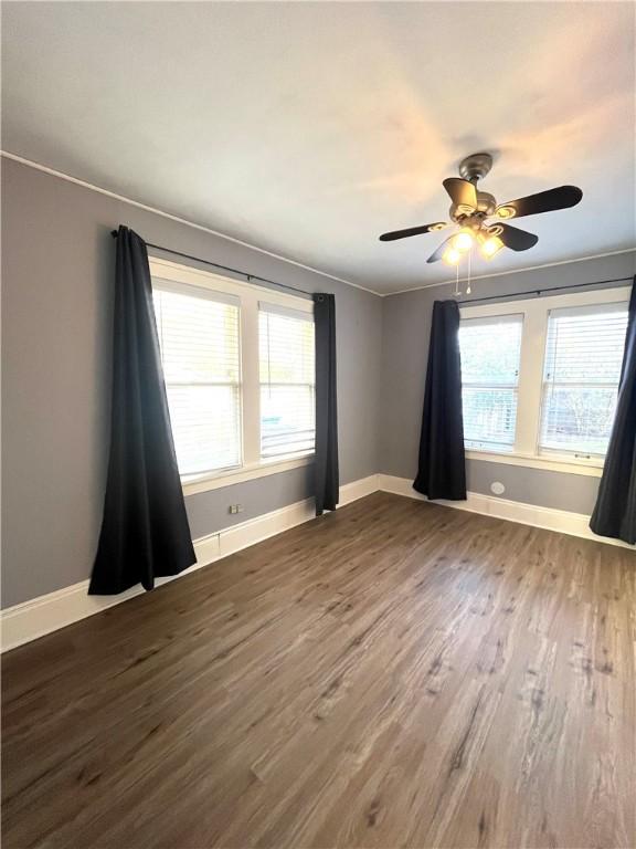 empty room with a ceiling fan, crown molding, baseboards, and dark wood-type flooring