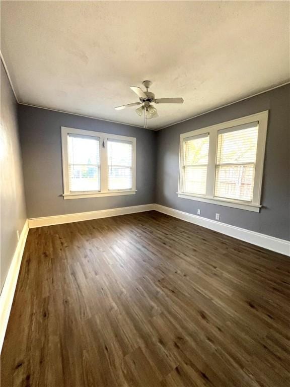 spare room featuring baseboards, dark wood finished floors, and a ceiling fan