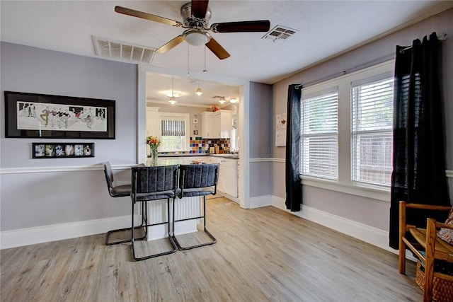 kitchen featuring light wood finished floors, a kitchen bar, visible vents, and white cabinetry