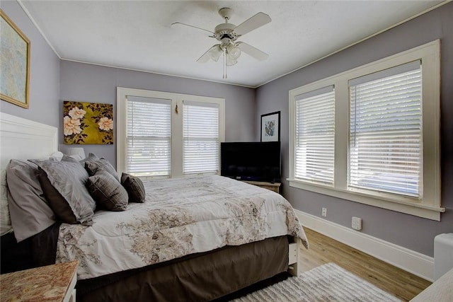 bedroom with ceiling fan, multiple windows, baseboards, and wood finished floors