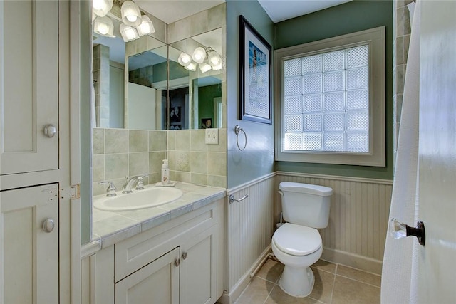 full bath with toilet, tile patterned flooring, vanity, and wainscoting