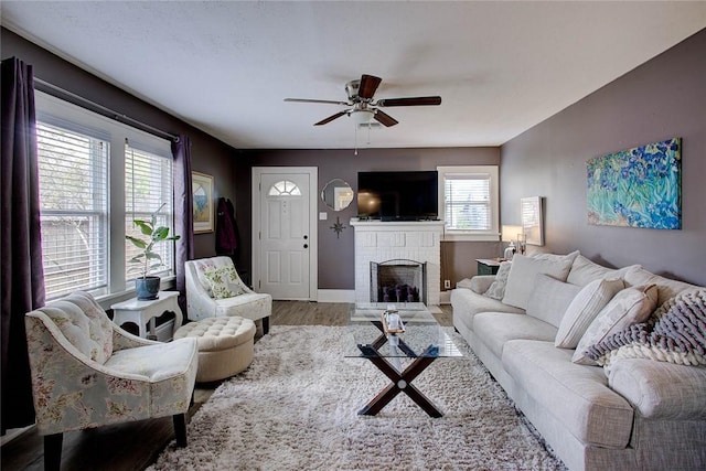 living room with ceiling fan, a fireplace, wood finished floors, and baseboards