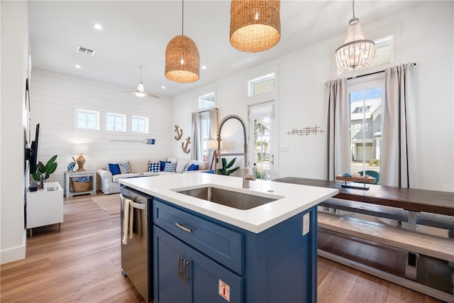 kitchen featuring a center island with sink, blue cabinets, sink, stainless steel dishwasher, and decorative light fixtures