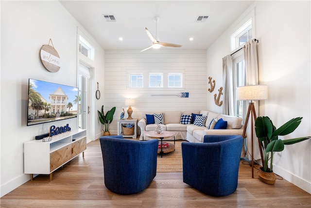 living room featuring ceiling fan, hardwood / wood-style floors, and wooden walls