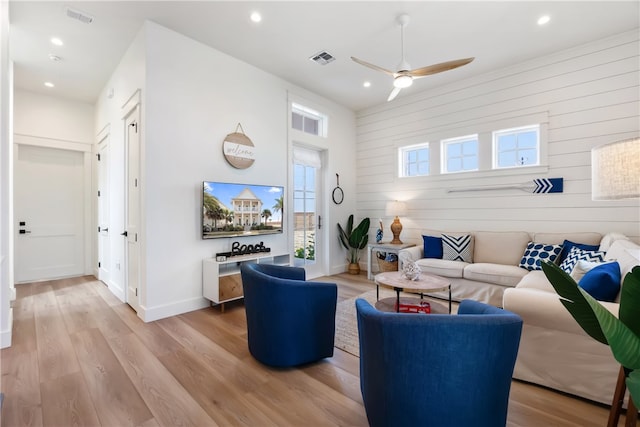 living room featuring ceiling fan, light hardwood / wood-style flooring, and wooden walls