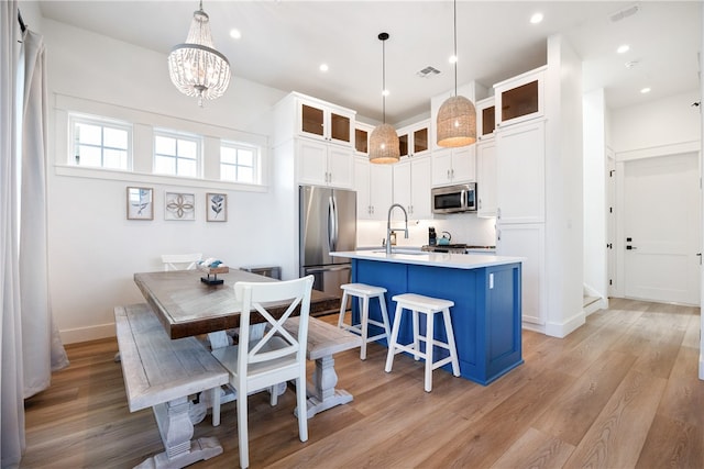 kitchen featuring appliances with stainless steel finishes, light wood-type flooring, a center island with sink, and decorative light fixtures