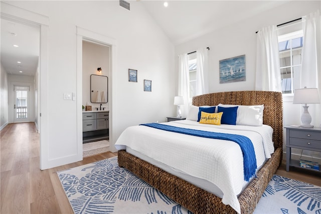 bedroom featuring vaulted ceiling, light wood-type flooring, multiple windows, and ensuite bath