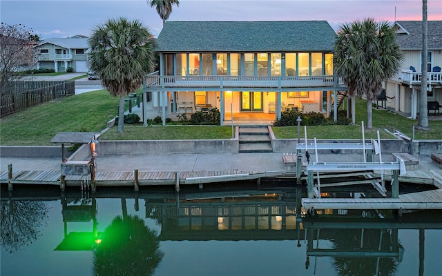 back house at dusk featuring a lawn and a water view