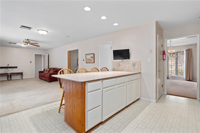 kitchen with white cabinetry, light carpet, a breakfast bar, and ceiling fan with notable chandelier