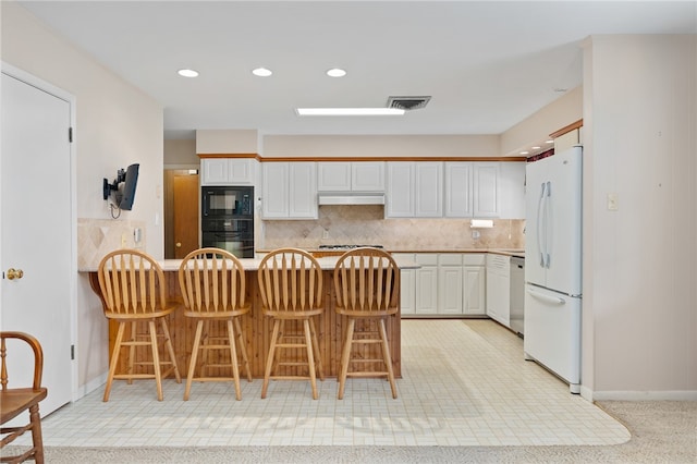 kitchen with white cabinets, kitchen peninsula, black appliances, tasteful backsplash, and a kitchen breakfast bar