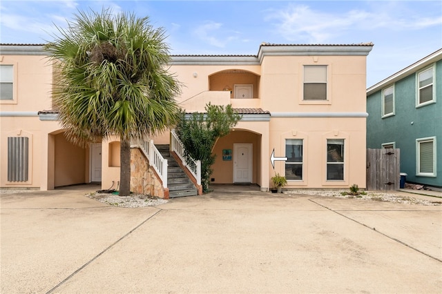 view of front facade with stairs, driveway, a tiled roof, and stucco siding