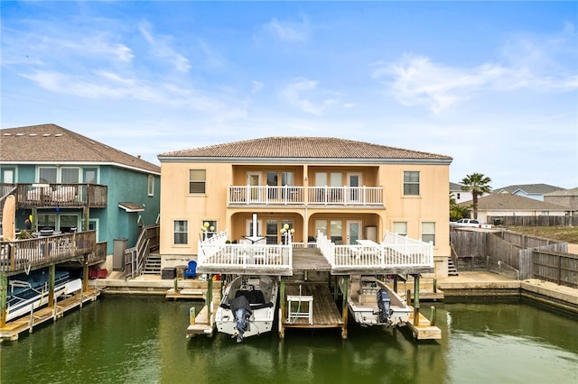 rear view of house featuring a water view, a balcony, boat lift, and stucco siding