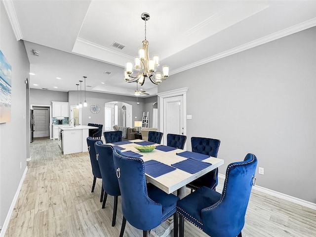 dining space with sink, a chandelier, light hardwood / wood-style flooring, ornamental molding, and a tray ceiling