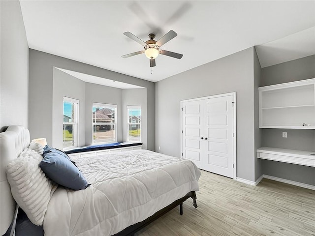 bedroom with built in desk, light hardwood / wood-style flooring, a closet, and ceiling fan